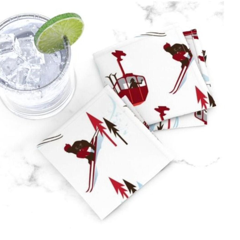 Vintage red and brown skiers and trees on cocktail napkins next to a cocktail